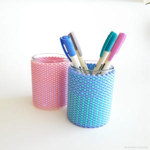 May include: Two glass pencil holders with beaded covers. One holder is pink and white, the other is blue and green. The holders are filled with pens.