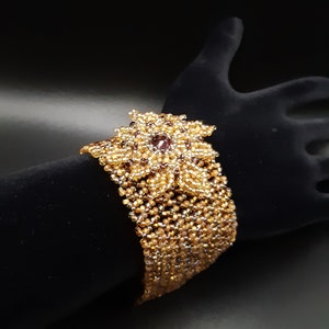 Bracciale con Flower Focal con Cristallo Swarovski nei toni viola ametista, oro e topazio e chiusura a scatola decorata. Polsino intrecciato di perline S-457