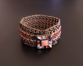 Bracelet manchette en filet de bronze avec fermoir bouton en émail coloré. Manchette tissée en perles de style antique avec lignes rouges, bleu encre et orange foncé. S-499