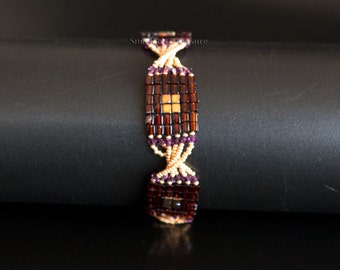 Bracelet perlé avec carrés de miel foncé et d’iris doré, cristaux Swarovski en violet améthyste et perles de graines torsadées d’or.  Fermoir carré S224