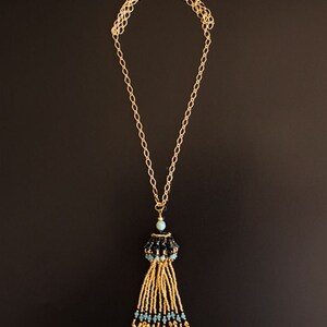 May include: A gold chain necklace with a black and blue beaded tassel pendant.