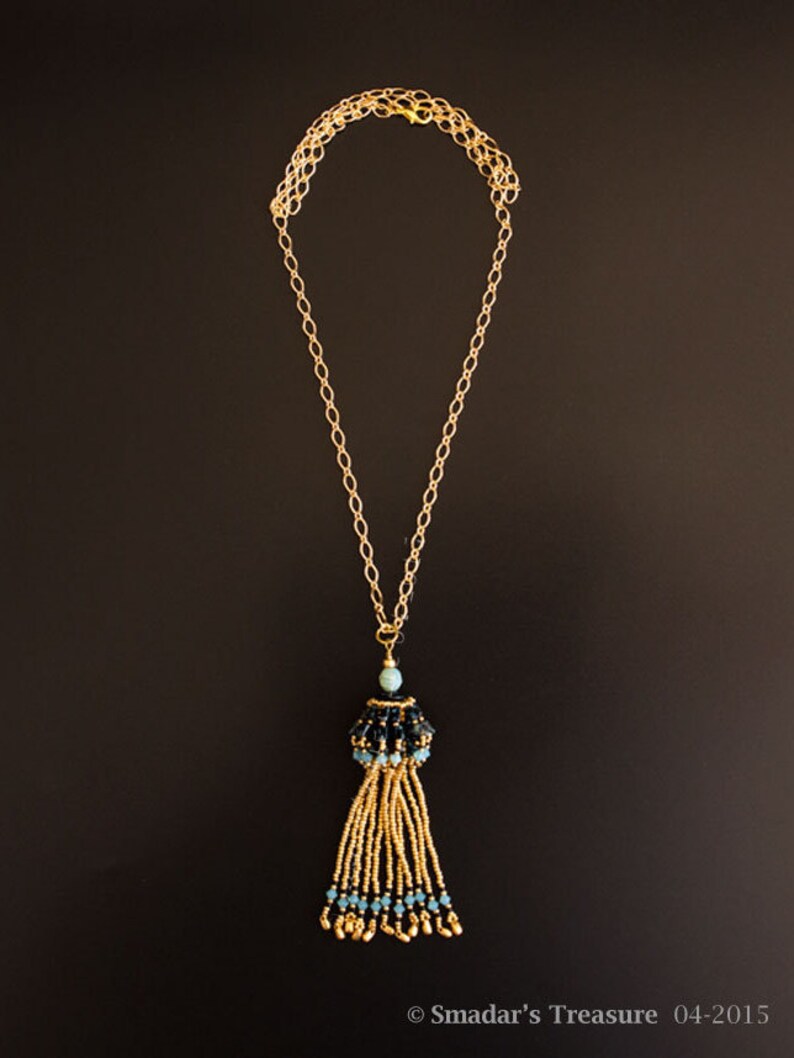 May include: A gold chain necklace with a black and blue beaded tassel pendant.