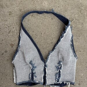May include: A denim halter top with a V-neckline and frayed edges. The top is made of a light blue denim fabric and has a dark blue trim.