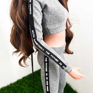 May include: Gray cropped hoodie and matching leggings with black side stripes and white text that reads "YOUR HANDS", "WITH SMARTDOLL", "THE FUTURE IS IN", and "THE FUTURE IS IN YOUR HANDS".
