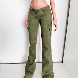 Puede incluir: Pantalones cargo verde oliva con bolsillos laterales y cierre de botón. Los pantalones tienen una pernera acampanada y se combinan con zapatillas blancas. La muñeca también lleva un top corto negro.