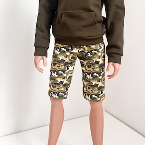 Puede incluir: Una sudadera con capucha verde con un bolsillo canguro y pantalones cortos de estampado de camuflaje.