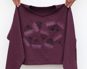 May include: A long-sleeved, plum-colored shirt featuring a floral design. The design consists of black stems and pink dotted flower heads. The shirt is held up against a white background, showcasing the garment's color and print.