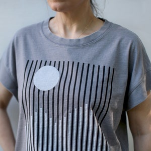 May include: A gray t-shirt with a black and white graphic design of vertical lines and a white circle.