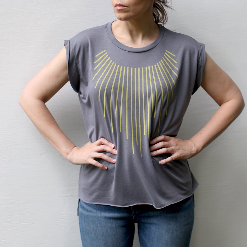 K&ouml;nnte beinhalten: Ein graues T-Shirt mit einem gelben geometrischen Design, das einem Halsband &auml;hnelt.