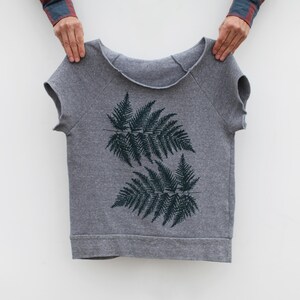 Puede incluir: Sudadera gris de manga corta con un dise&ntilde;o de hojas de helecho verde oscuro. La parte superior con cuello redondo tiene un ajuste relajado y est&aacute; hecha de un material suave. El dise&ntilde;o de helecho est&aacute; centrado en la parte delantera.
