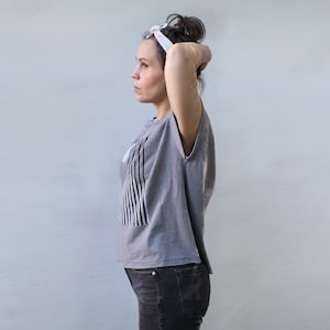 May include: A woman wearing a gray sleeveless shirt with a black and white striped design, black jeans, and a white headband.