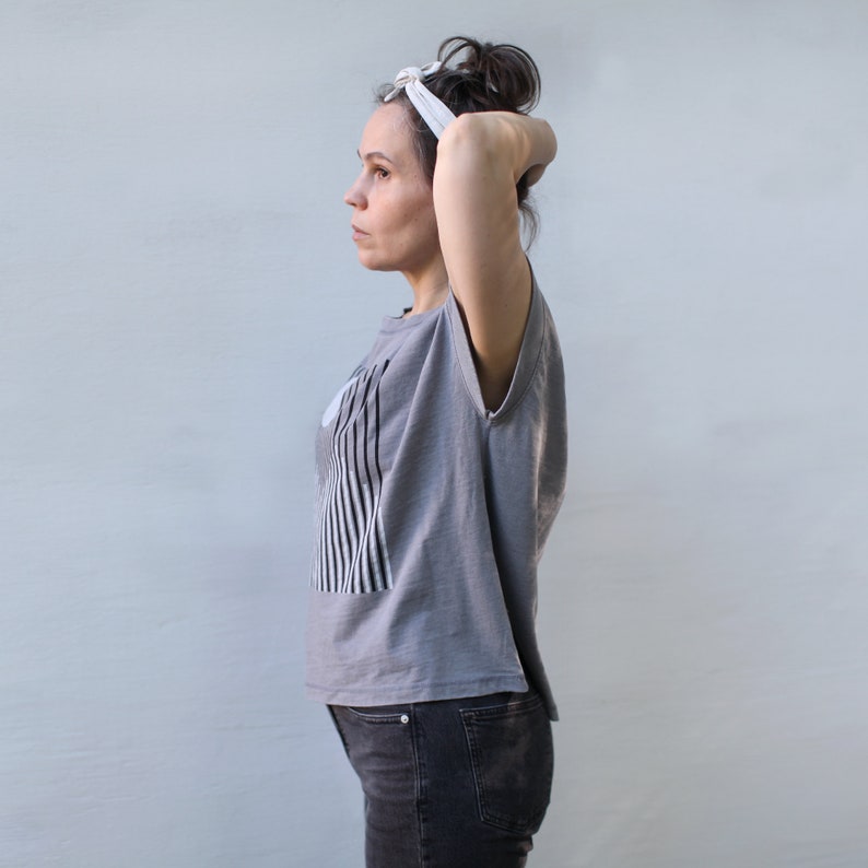 May include: A woman wearing a gray sleeveless shirt with a black and white striped design, black jeans, and a white headband.