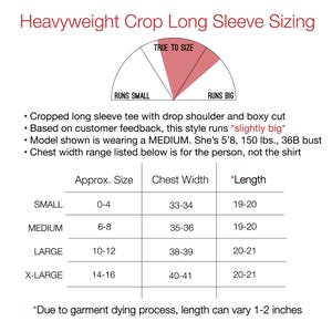 May include: Image of a sizing chart for a heavyweight crop long sleeve tee. The chart includes approximate sizes, chest width in inches, and length in inches. The text indicates the style runs slightly big.