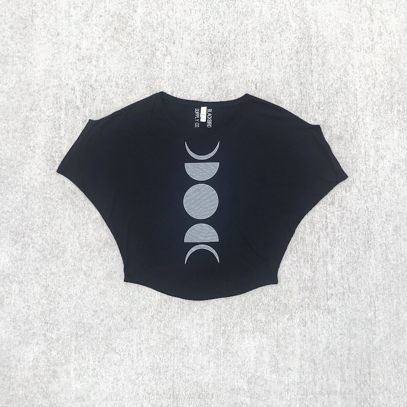 May include: Black short-sleeved t-shirt with a white moon phases design. The shirt has a relaxed fit and a slightly cropped hem. The text "BLACK MOON SUPPLY CO." is printed on the back of the neck.