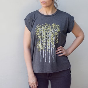 Może przedstawiać: Szary t-shirt z białym i ż&oacute;łtym nadrukiem graficznym przedstawiającym grupę drzew. Drzewa mają białe pnie i ż&oacute;łte liście.