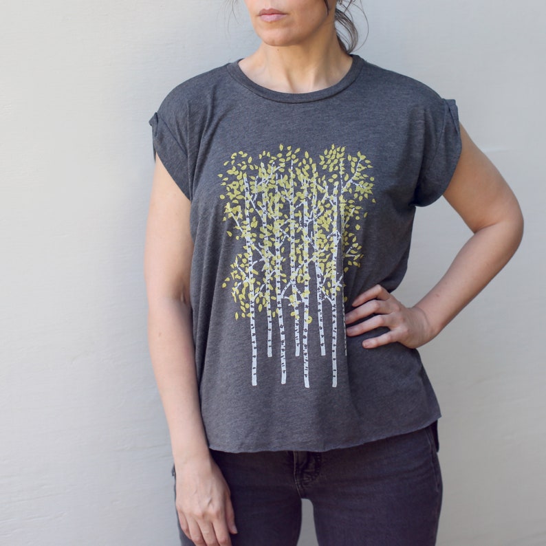 Może przedstawiać: Szary t-shirt z białym i ż&oacute;łtym nadrukiem graficznym przedstawiającym grupę drzew. Drzewa mają białe pnie i ż&oacute;łte liście.