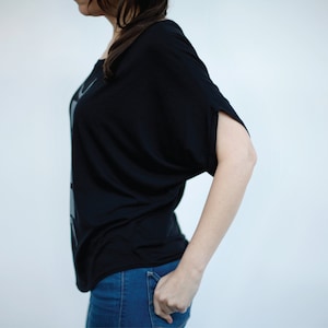 May include: A woman wearing a black, loose-fitting shirt with a gray graphic design and blue jeans.