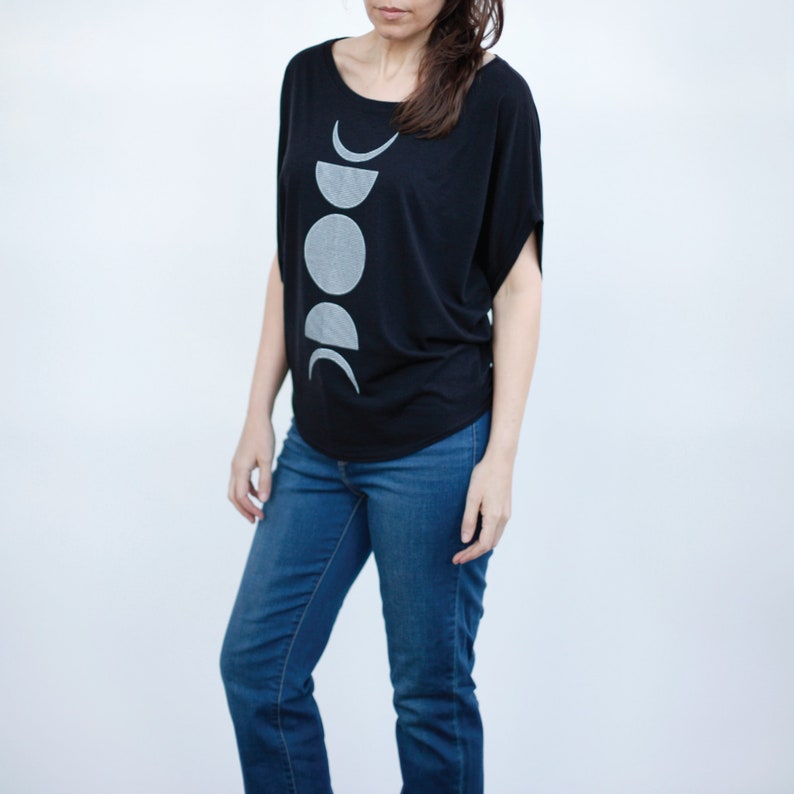 May include: A black t-shirt with a white moon phases graphic print. The shirt has a relaxed fit and a scoop neck.