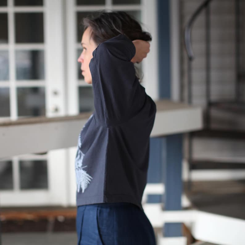 May include: A dark navy long-sleeve shirt with a light blue graphic design on the front. The shirt is paired with dark blue pants. The image is taken in natural light, with a blurred background.