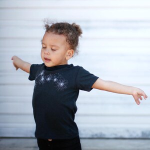 May include: A child wearing a black t-shirt with the Little Dipper constellation screen-print on the front.