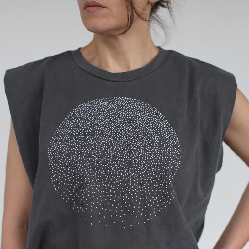 Op de afbeelding: Een mouwloos shirt in antracietgrijs met een wit cirkelvormig ontwerp gemaakt van kleine stippen. Het shirt heeft een losse pasvorm en een ronde hals.