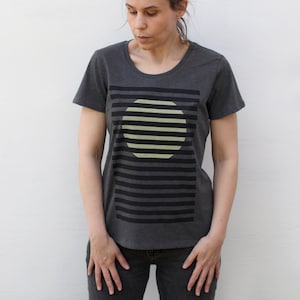 May include: A dark gray t-shirt with a graphic print of a yellow circle with black stripes on a black and white striped background.