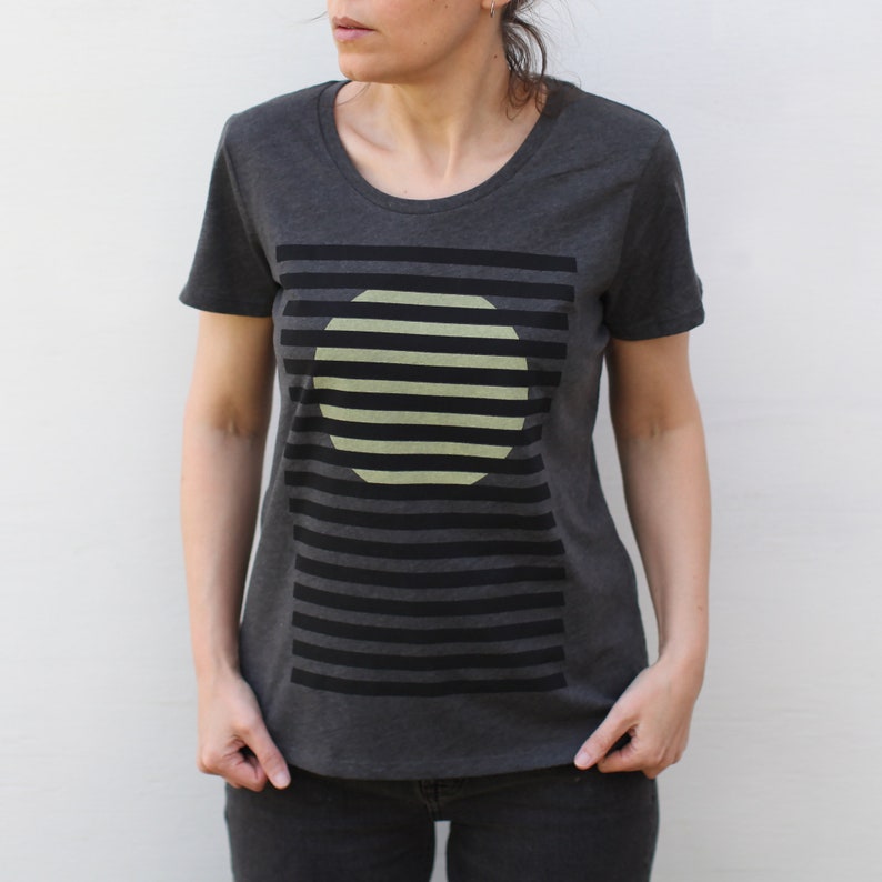 May include: A dark gray t-shirt with a graphic design of a light green circle with black stripes on a black and white striped background.