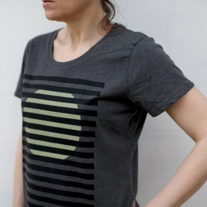 May include: A dark gray t-shirt with a graphic design of a circle with black stripes on it. The circle is partially obscured by the stripes.