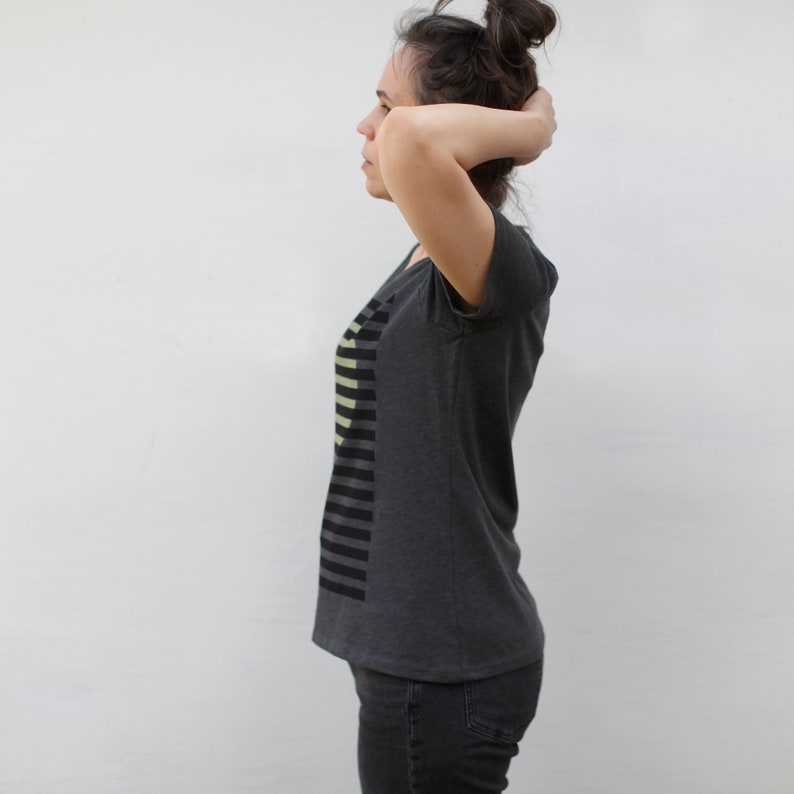 May include: A dark grey t-shirt with a black and light yellow striped design on the left side of the shirt.