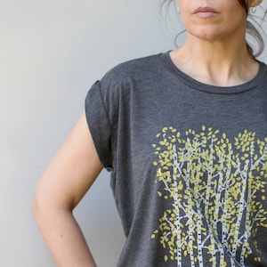 Może przedstawiać: Szary t-shirt z nadrukiem graficznym przedstawiającym grupę drzew z ż&oacute;łtymi liśćmi. Drzewa są stylizowane i mają białe pnie.