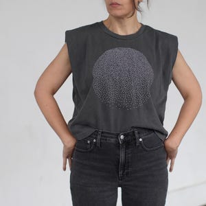 Op de afbeelding: Een mouwloos t-shirt in antracietgrijs met een wit cirkelvormig ontwerp gemaakt van kleine stippen. Het shirt heeft een ontspannen pasvorm en een licht ingekorte lengte.