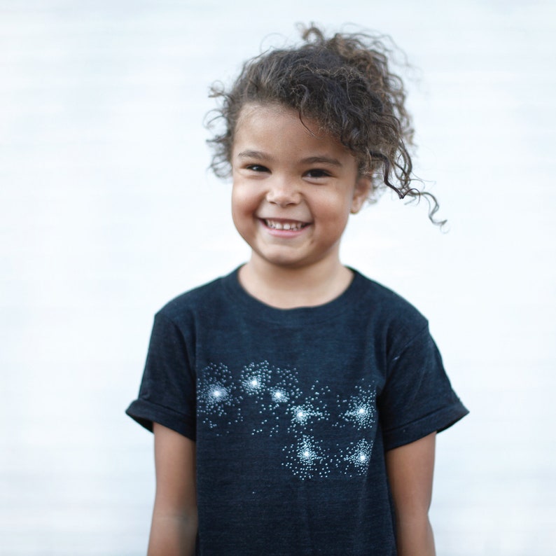 May include: A girl wearing a Big Dipper constellation t-shirt in heather black.