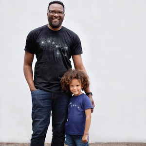 May include: A father and a child wearing black and indigo blue t-shirts with Big and Little Dipper constellation designs.