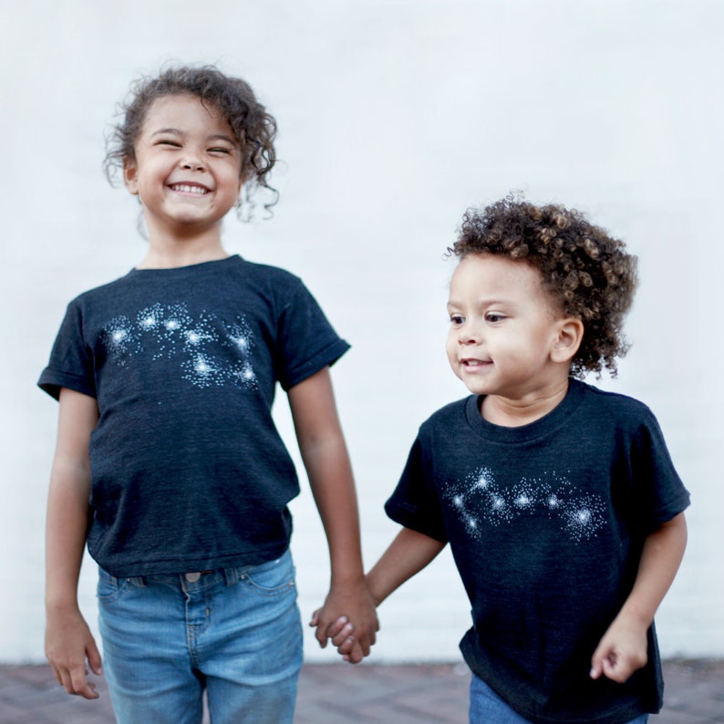 May include: Two sisters wearing matching Big and Little Dipper constellation t-shirts.