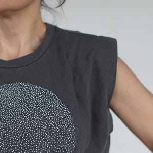 Op de afbeelding: Een grijs, mouwloos shirt met een wit gestippeld ontwerp in de vorm van een halve cirkel.
