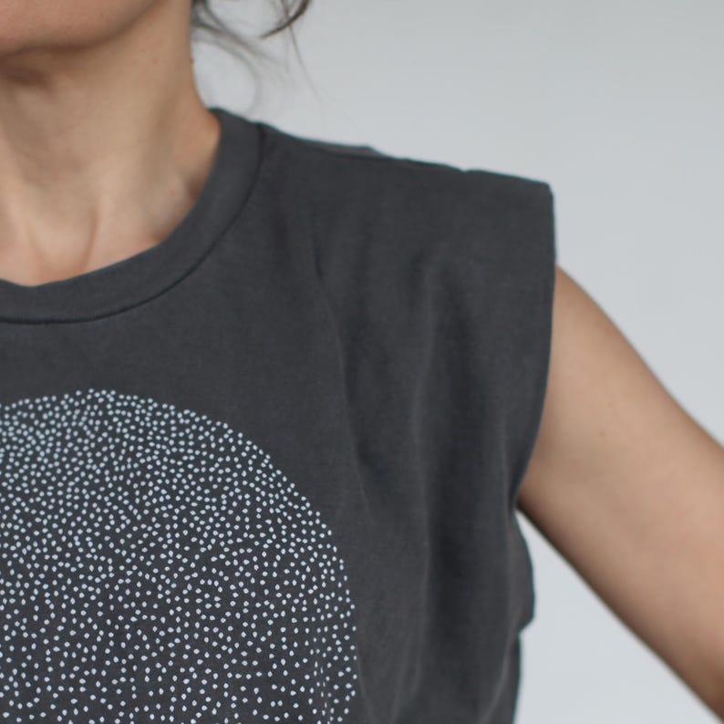 Op de afbeelding: Een grijs, mouwloos shirt met een wit gestippeld ontwerp in de vorm van een halve cirkel.