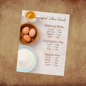 May include: A white card with brown text lists kitchen-inspired diffuser blends with essential oil recipes for Baking Bliss, Pumpkin Pie, and Apple Pie. The card is on a wooden surface with a bowl of flour and a bowl of eggs.