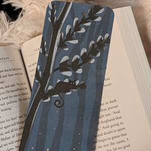 May include: A blue and black bookmark with a tree and a bird silhouette. The bookmark is made of paper and has a textured surface. The background is a dark blue with white stars.