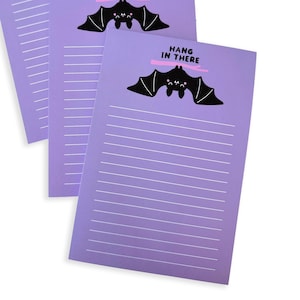 May include: Three purple lined notepad sets with a black bat illustration and the text "Hang in there" in pink.
