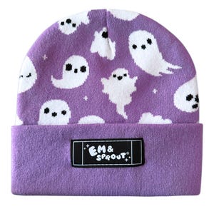 Puede incluir: Un gorro morado con un estampado de fantasmas blancos. El gorro tiene un borde doblado y una etiqueta rectangular negra con el texto "EM & SPROUT". Los fantasmas tienen ojos negros y est&aacute;n repartidos por el gorro.
