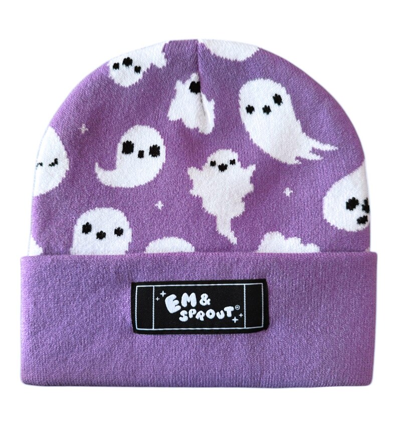Puede incluir: Un gorro morado con un estampado de fantasmas blancos. El gorro tiene un borde doblado y una etiqueta rectangular negra con el texto "EM & SPROUT". Los fantasmas tienen ojos negros y est&aacute;n repartidos por el gorro.