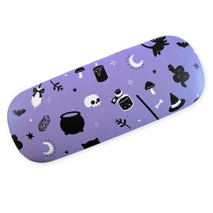 Peut inclure: Un étui rigide rectangulaire aux bords arrondis de couleur violet clair, orné d'un motif répétitif d'icônes noires et blanches représentant un chaudron, un crâne, un serpent, un chapeau de sorcière, un balai, une bougie, une lune, des étoiles, des champignons et des fioles.