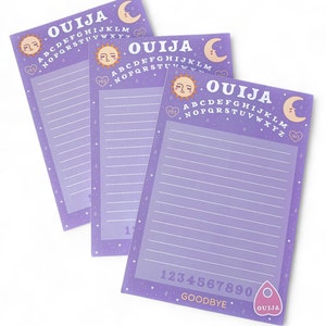May include: Three purple Ouija board notepads with a moon, sun, and stars design. Each notepad has the alphabet, numbers 1-9, and the words "YES", "NO", and "GOODBYE".