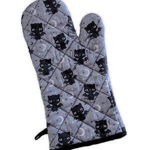 May include: A gray quilted oven mitt with a black bat cat pattern. The mitt has a black hanging loop and a black trim.