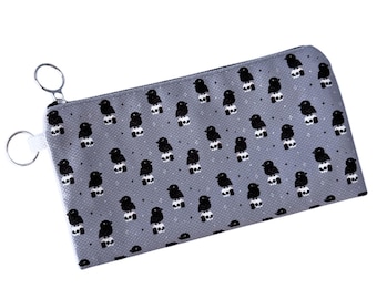 May include: A gray zippered pouch with a repeating pattern of black birds holding white skulls. The pouch has two silver zipper pulls.