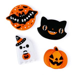 Peut inclure: Quatre breloques en silicone sur le th&egrave;me d'Halloween&nbsp;: un chat noir avec des dents orange, un fant&ocirc;me blanc avec un chapeau de sorci&egrave;re et une citrouille, une citrouille orange avec un visage de citrouille sculpt&eacute;e et une chauve-souris avec des ailes orange et le texte&nbsp;&laquo;&nbsp;Stay Spooky&nbsp;&raquo;.
