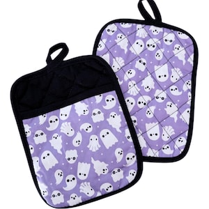 May include: A pair of purple and black oven mitts with a ghost pattern. The mitts are quilted and have a hanging loop.