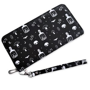 May include: Black wallet with a wrist strap, featuring a repeating white pattern of potion bottles, mushrooms, skulls, bats, and crescent moons. The wallet has a silver-colored zipper and clasp.