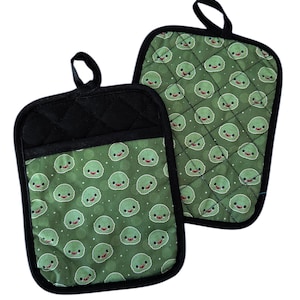 May include: A pair of green and black oven mitts with a cute cartoon character pattern. The mitts are quilted and have a black trim.
