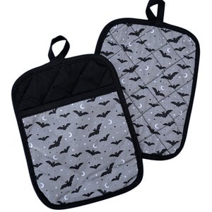 May include: A pair of black and gray oven mitts with a bat and crescent moon pattern. The mitts are quilted and have a black trim.